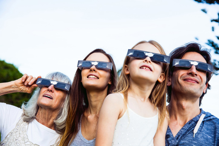 grandmother, daughter, grandaughter and man with glasses protecting eyes from solar eclipse