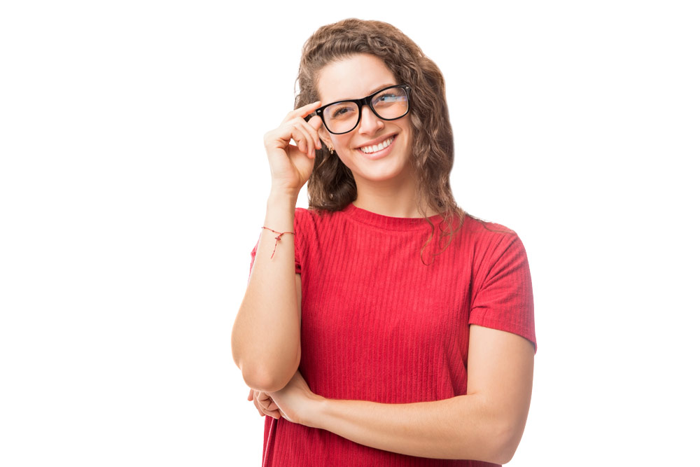 Smiling woman in a red shirt touching her glasses, standing against a white background.