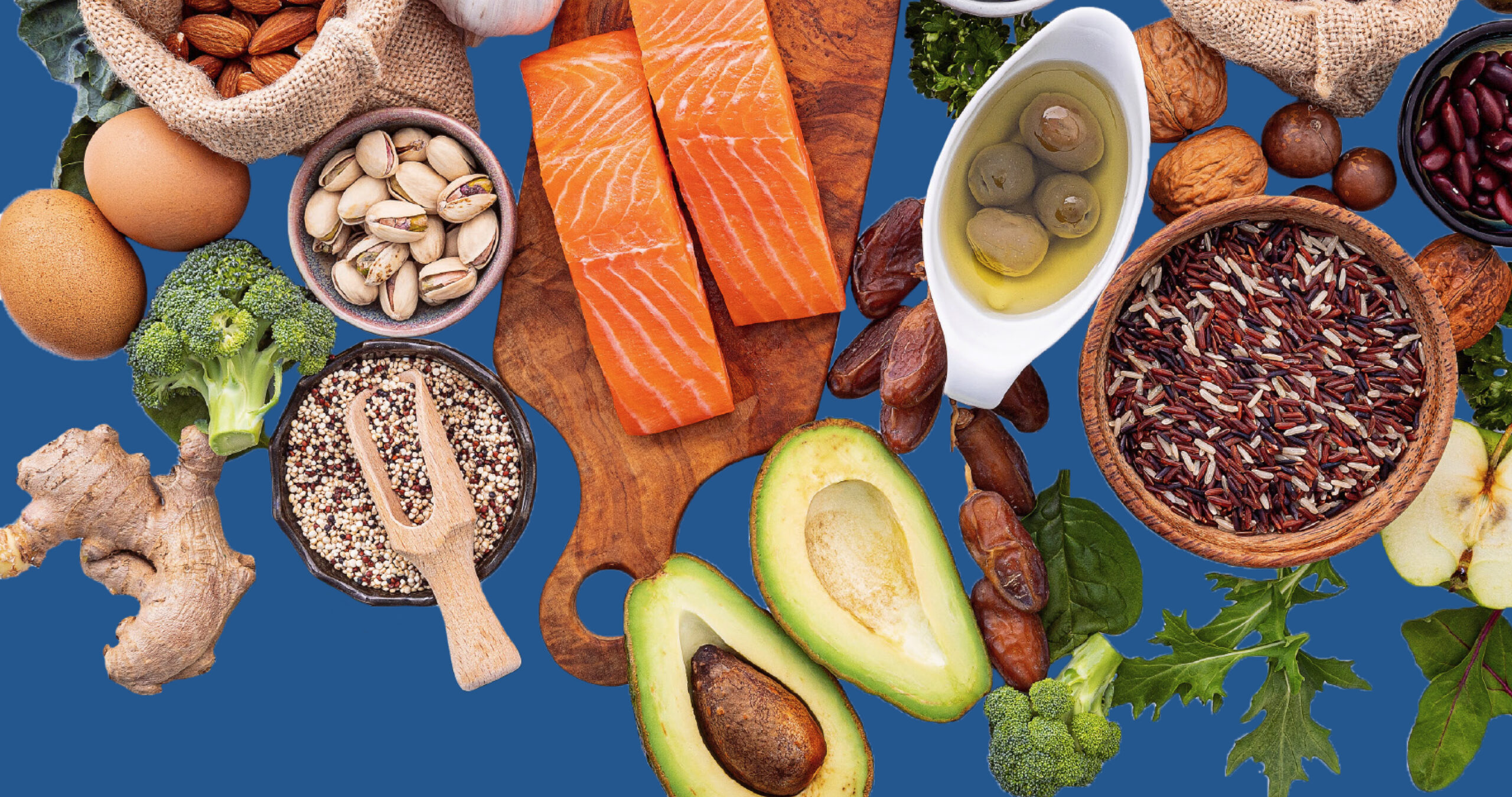 Assorted healthy foods including salmon, avocado, nuts, eggs, rice, olives, and vegetables on a blue background.